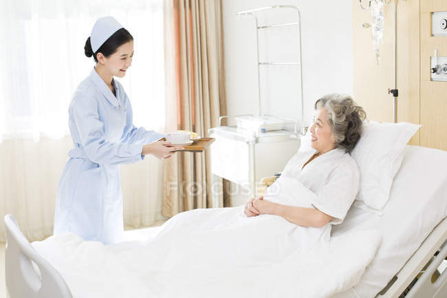 Enfermeira chinesa servindo comida para paciente sênior — Fotografia de Stock