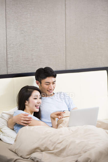 Casal chinês usando laptop na cama — Fotografia de Stock