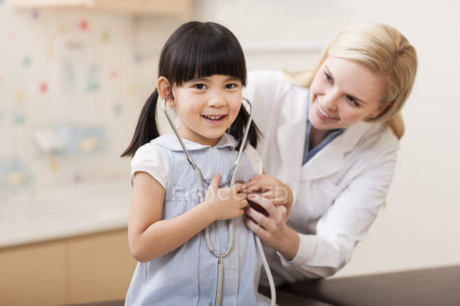 Female doctor playing with girl with stethoscope — Stock Photo