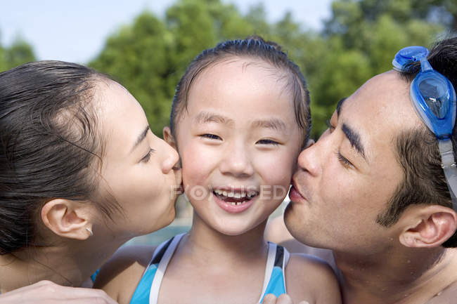 Chinese parents kissing daughter at poolside — Stock Photo