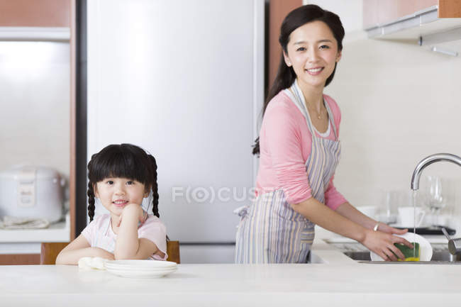 Chinese mother and daughter washing dishes in kitchen — Stock Photo