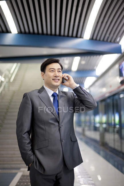 Homme d'affaires chinois parlant au téléphone au quai du métro — Photo de stock