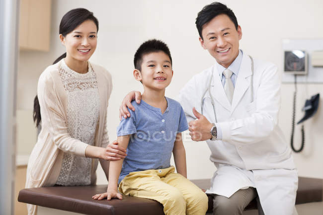 Médico chino con niño y mujer en el hospital haciendo pulgares hacia arriba - foto de stock