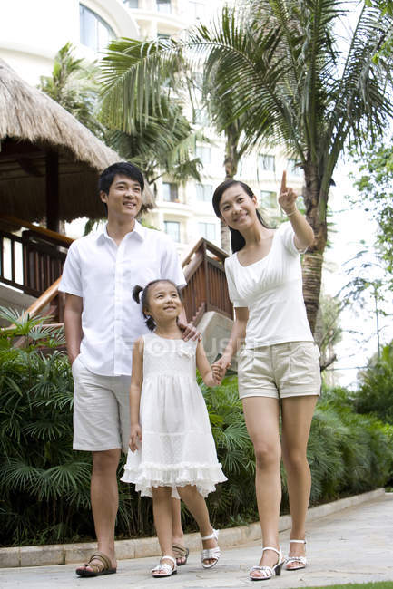 Chinese parents with daughter standing and pointing at tourist resort — Stock Photo