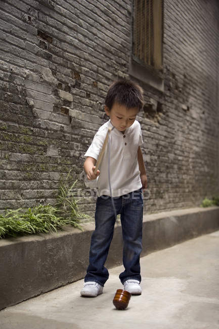 Chinese boy playing with spinning top in alley — Stock Photo