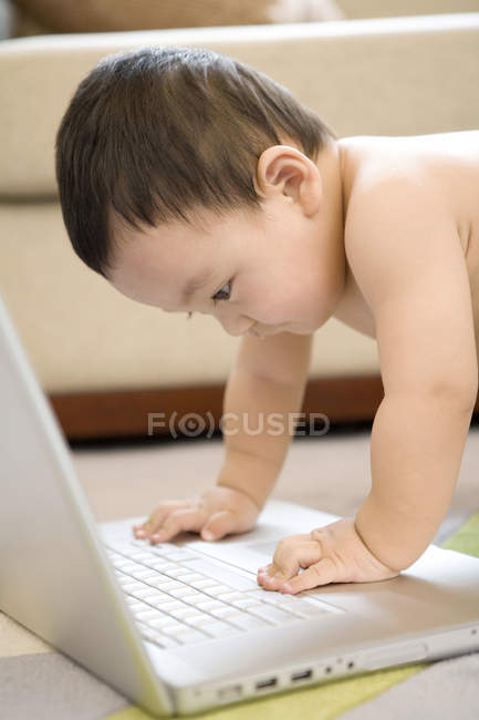 Chinesisches Kleinkind sitzt auf dem Boden und schaut auf Laptop — Stockfoto