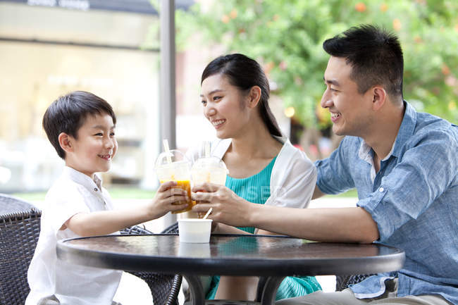 Padres chinos con hijo disfrutando de bebidas frías en la cafetería de la acera - foto de stock