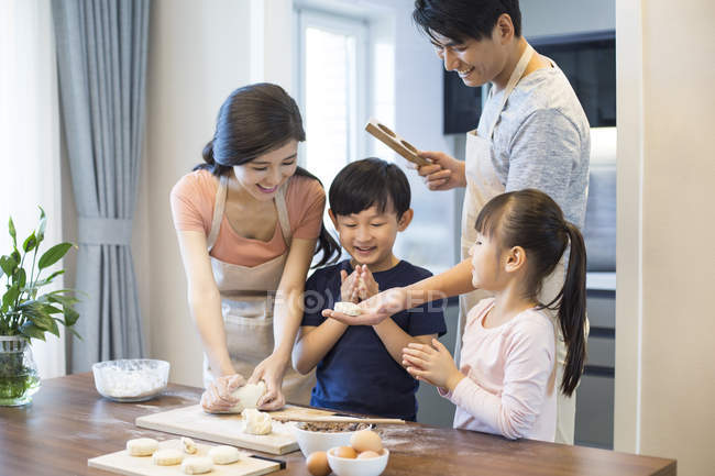Familia china con hermanos horneando juntos en la cocina - foto de stock