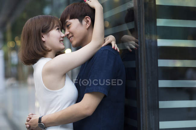 Young Chinese couple leaning on shop window and embracing on street — Stock Photo