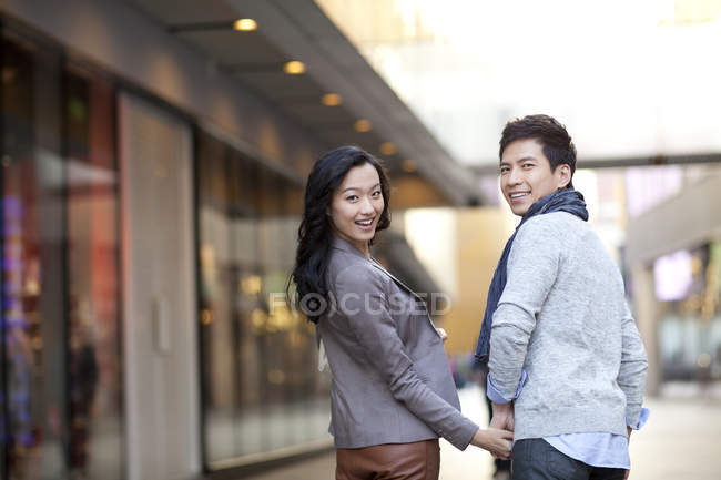 Chinese couple holding hands on city street and looking back, rear view — Stock Photo