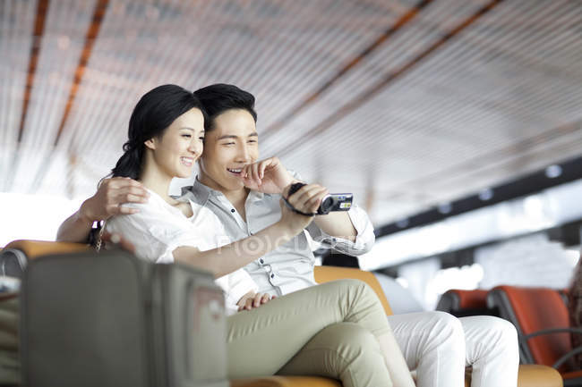 Chinese couple looking at digital camera in airport lounge — Stock Photo