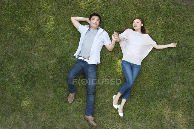 Вид сверху на лежащую на траве молодую китайскую пару — стоковое фото