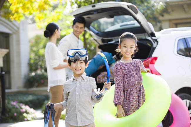 Chinese siblings with water sports equipment posing in front of car and parents — Stock Photo