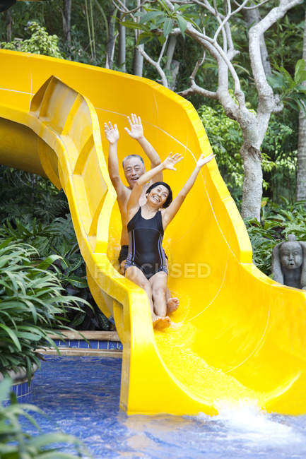 Senior Chinese couple riding on water slide — Stock Photo