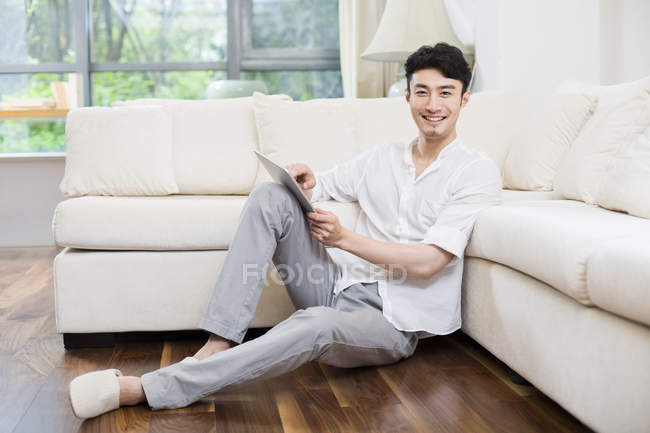 Chinese man using digital tablet on floor in living room — Stock Photo