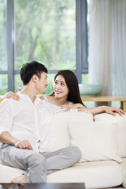 Jeune couple chinois souriant et se regardant sur le canapé — Photo de stock