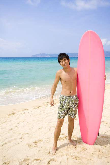 Joven chino sosteniendo tabla de surf rosa - foto de stock
