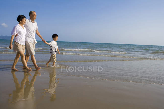Abuelos chinos y nieto caminando por la playa - foto de stock