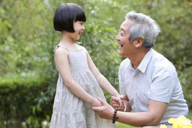 Chinese grandpa and granddaughter holding hands in garden — Stock Photo