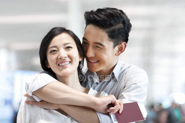 Casal chinês abraçando no aeroporto com bilhetes e passaporte — Fotografia de Stock