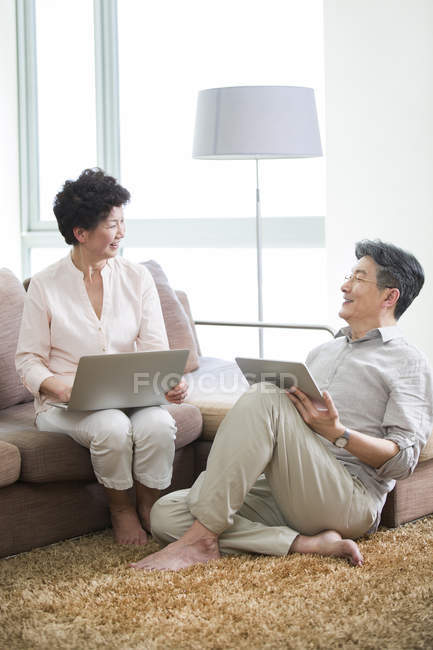 Chinois couple aîné avec ordinateur portable et tablette numérique parler dans le salon — Photo de stock