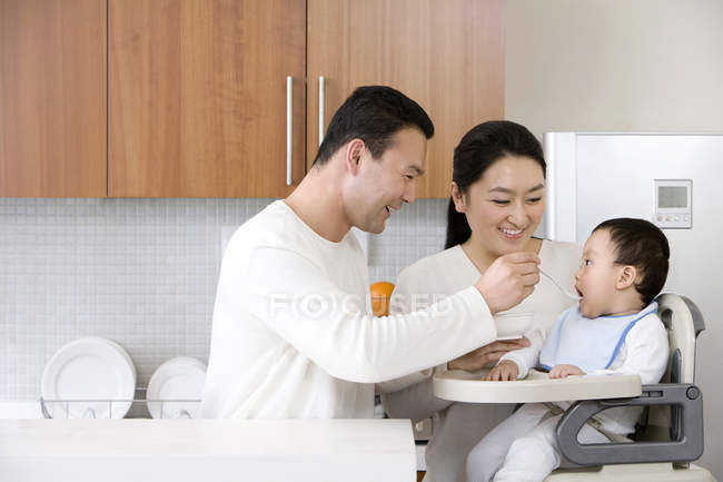 Padres chinos alimentando a bebé en silla alta - foto de stock