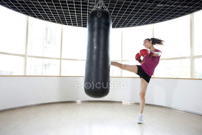 Chinese woman kicking punching bag — Stock Photo