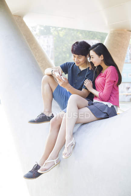 Chinese couple listening to music on smartphone on street — Stock Photo