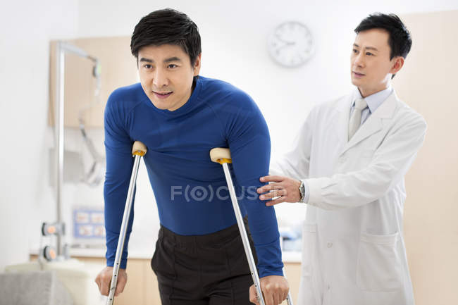 Médico chino ayudando al paciente con muletas - foto de stock