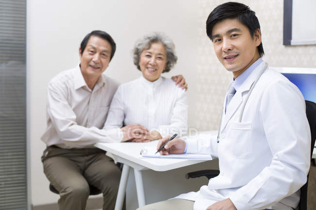 Médico chino sentado con pareja mayor en el hospital - foto de stock
