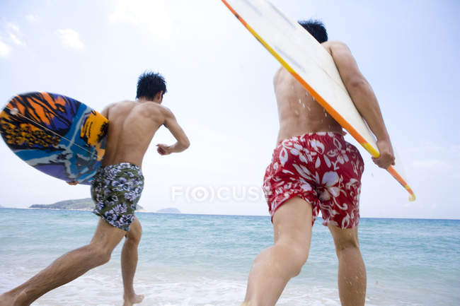 Male friends running with surfboards in sea water — Stock Photo