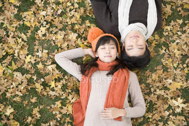 Chinese couple lying amongst maple leaves and sharing earphones — Stock Photo