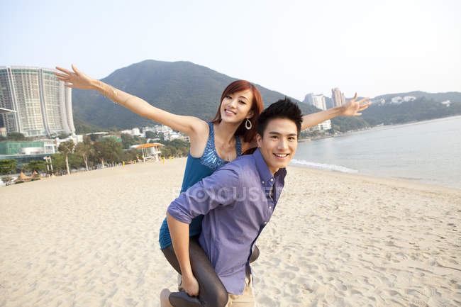 Chinese couple playing piggyback on beach of Repulse Bay, Hong Kong — Stock Photo