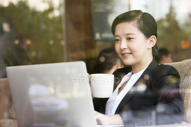 Chinesische Geschäftsfrau benutzt Laptop mit Tasse Kaffee — Stockfoto
