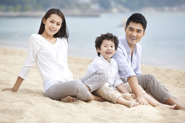 Padres chinos con hijo descansando en la playa y mirando en la cámara - foto de stock