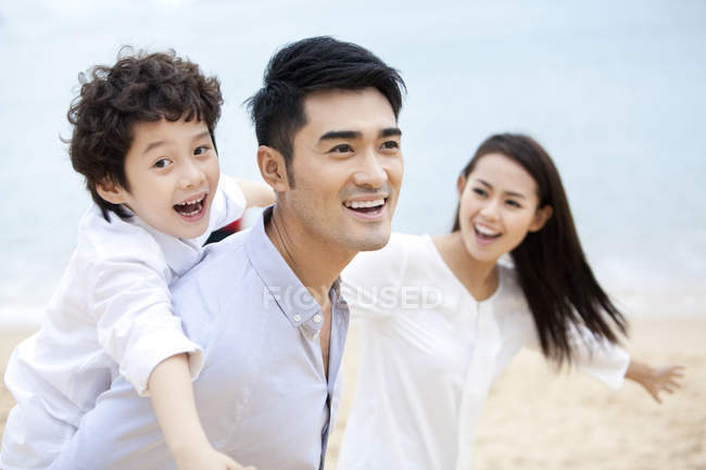 Китайский отец катает сына на спине по пляжу с матерью — стоковое фото