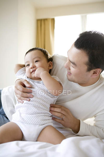 Chinese man holding infant son on bed — Stock Photo