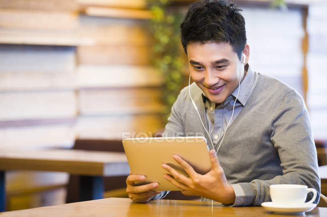Chinese man using digital tablet with earphones in coffee shop — Stock Photo