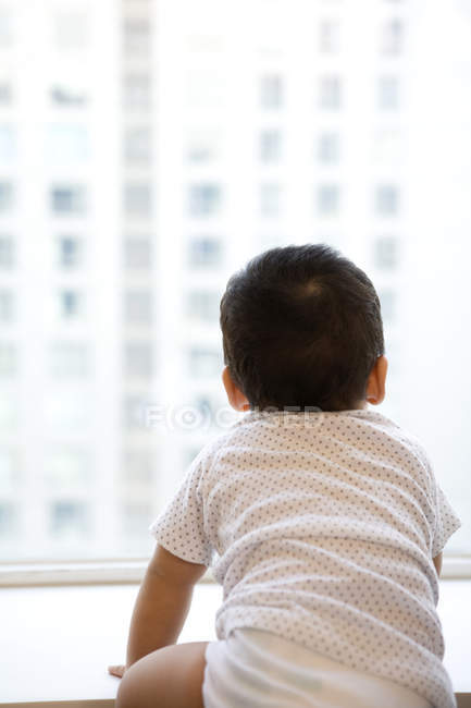 Infante mirando por la ventana, vista trasera - foto de stock