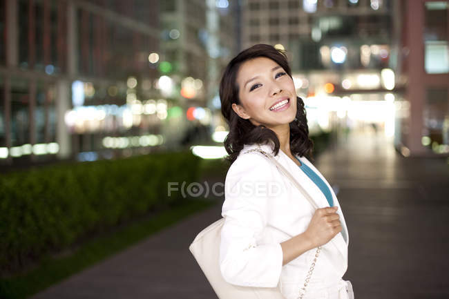 Mujer china con bolso de hombro de pie en la ciudad - foto de stock