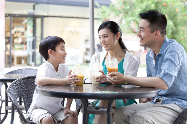 Китайские родители с сыном наслаждаются холодными напитками в кафе на тротуаре — стоковое фото