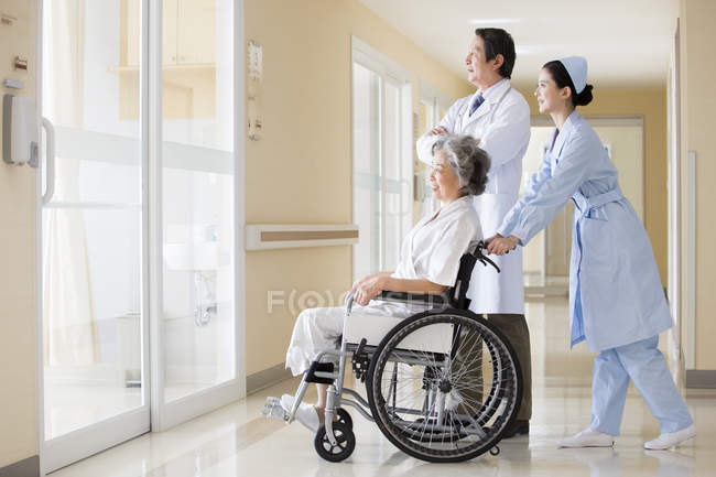 Trabalhadores médicos chineses cuidando de mulher idosa em cadeira de rodas — Fotografia de Stock