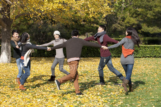Chinese young adults running in circle in park in autumn — Stock Photo
