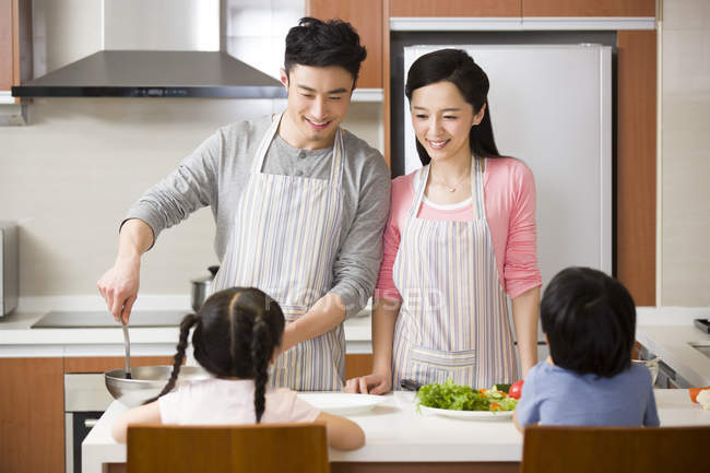 Padres chinos con niños cocinando en la cocina - foto de stock