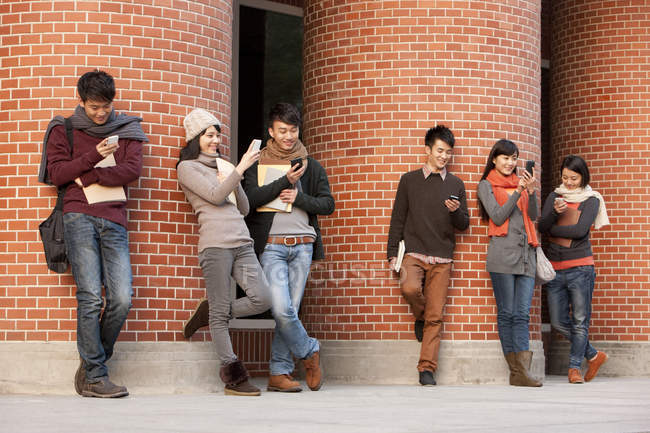 Estudantes universitários chineses jogando telefone inteligente na frente de um prédio universitário — Fotografia de Stock