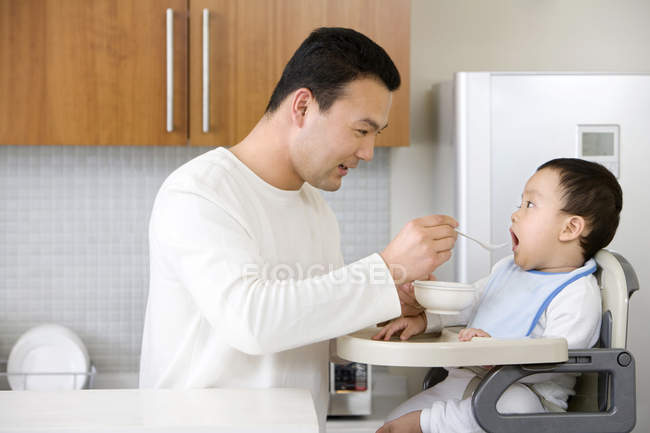 Uomo cinese alimentazione bambino ragazzo in seggiolone — Foto stock