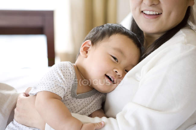 Mujer china sosteniendo al bebé en el pecho y sonriendo - foto de stock
