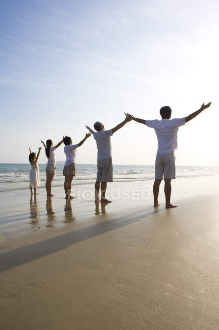Rückansicht einer Mehrgenerationenfamilie mit erhobenen Armen am Strand — Stockfoto