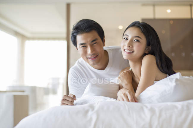 Casal chinês deitado na cama e olhando para a câmera — Fotografia de Stock
