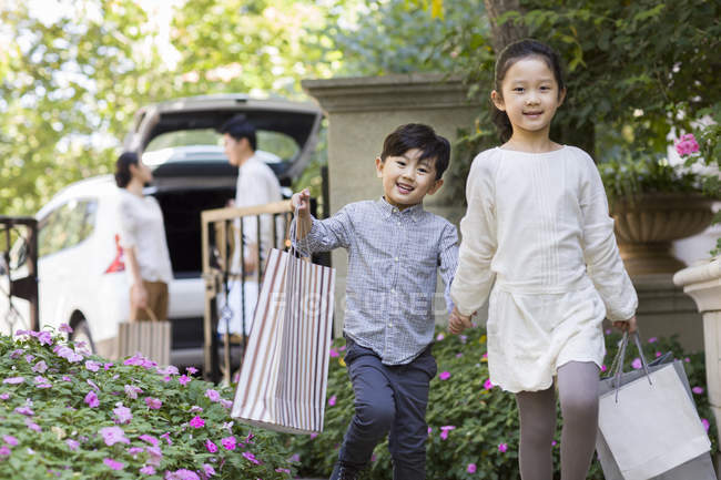 Hermano chino con bolsas de compras caminando en el patio - foto de stock